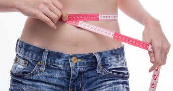 Woman checking stomach measurements with measuring tape