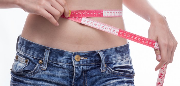 Woman checking stomach measurements with measuring tape