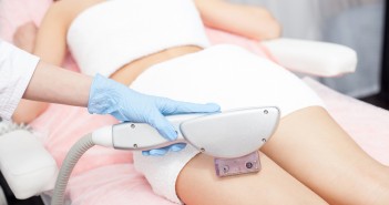 Close up of hand of professional beautician undergoing laser skin treatment on human legs. The woman is lying with relaxation. The cosmetologist is wearing a glove