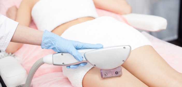 Close up of hand of professional beautician undergoing laser skin treatment on human legs. The woman is lying with relaxation. The cosmetologist is wearing a glove